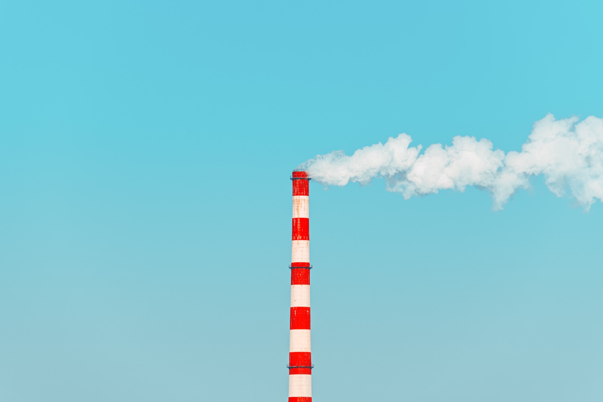 A tall red and white industrial smokestack against a clear blue sky