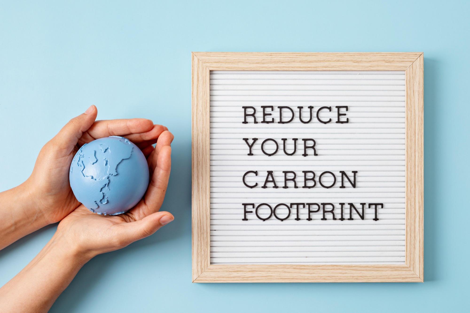 Hands holding a small globe next to a sign reading "Reduce Your Carbon Footprint"