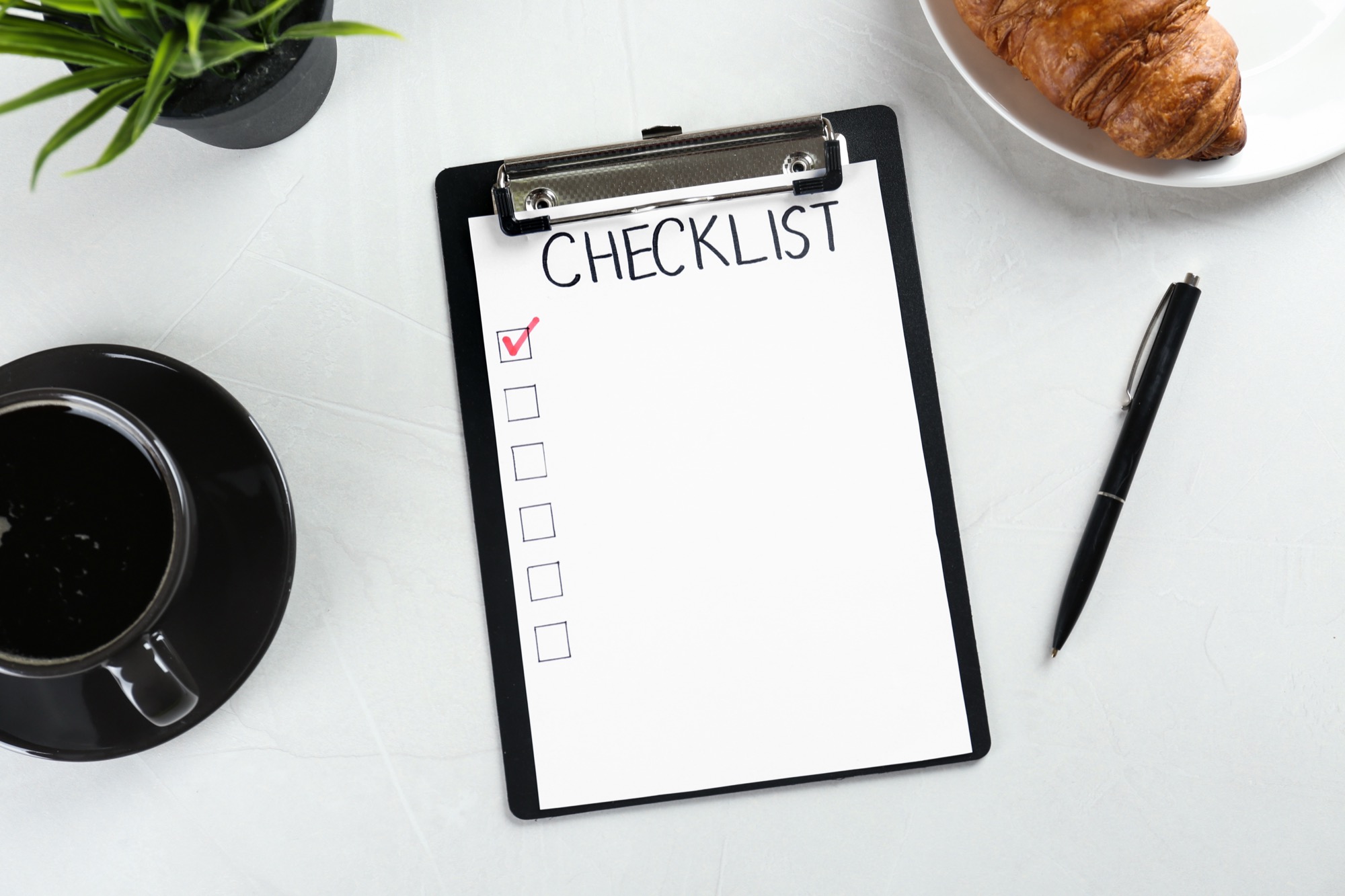 A handwritten "CHECKLIST" on a clipboard next to coffee and a croissant