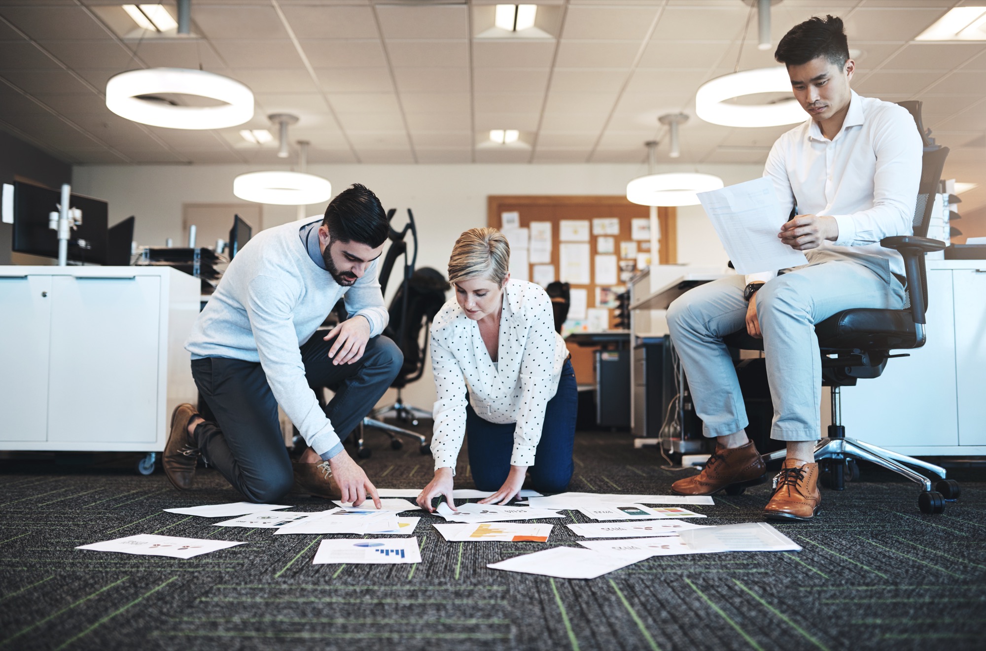 A business team reviewing data reports spread out on the office floor